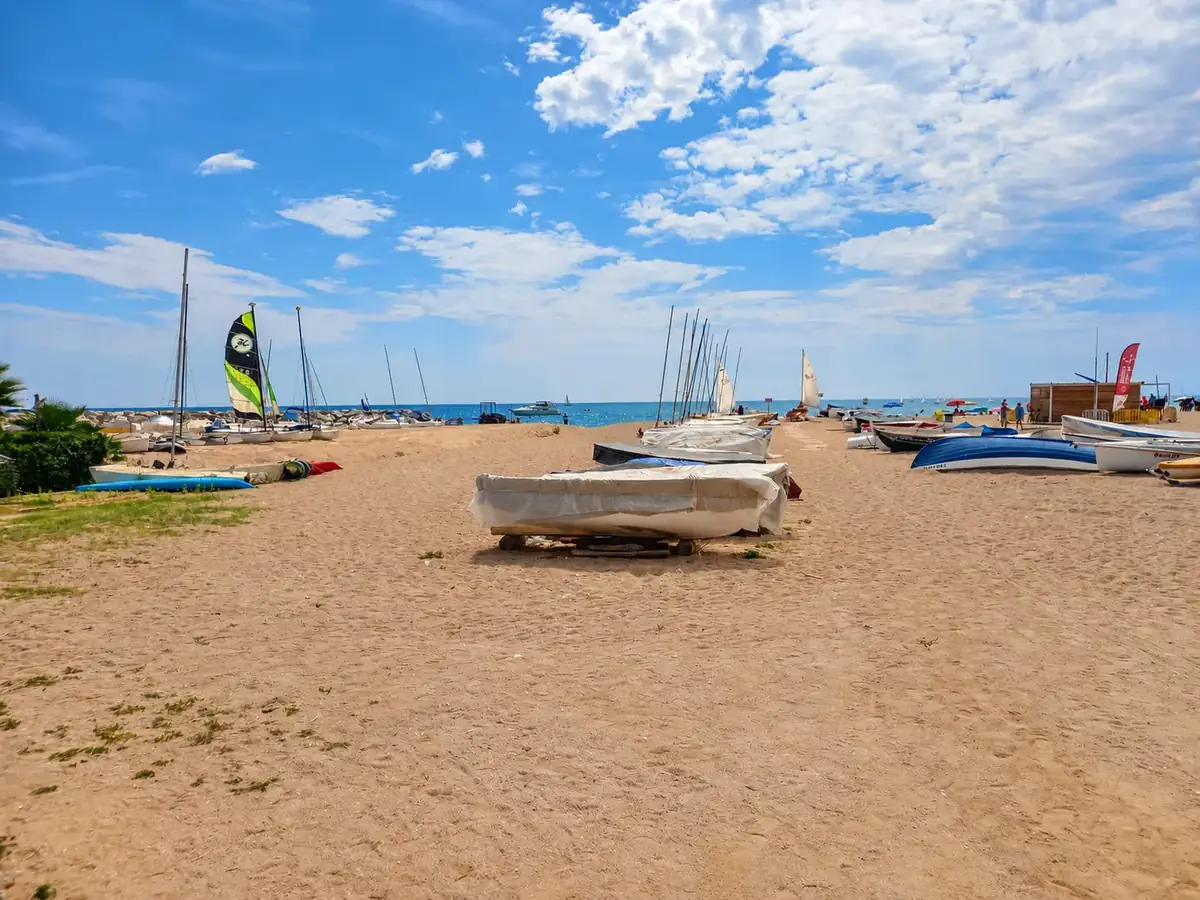 Barcas de vela sobre la arena de la Platja de les Barques, en Sant Pol de Mar, con el mar al fondo